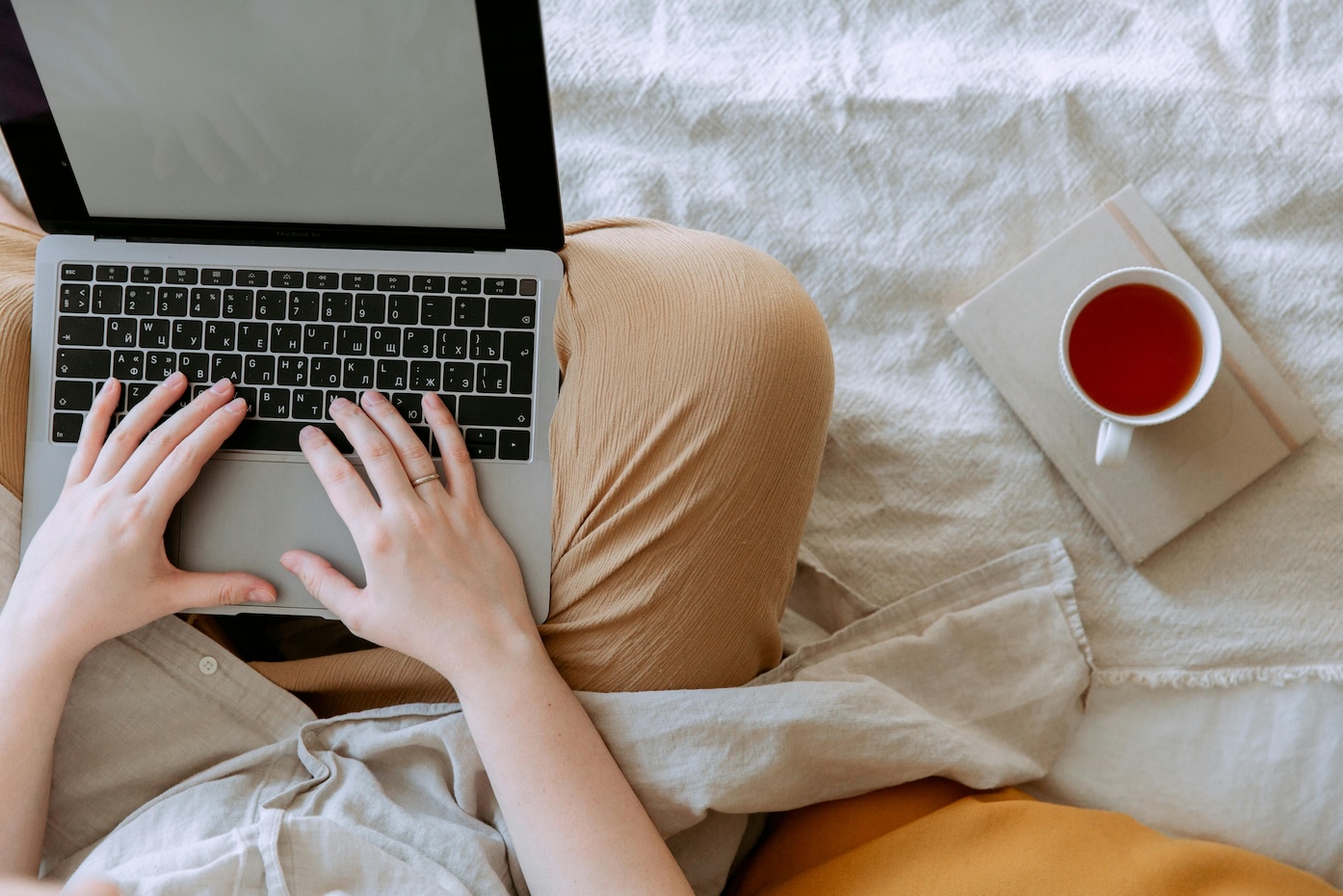 A photo of a person's lap with a laptop computer on their lap and tea next to them